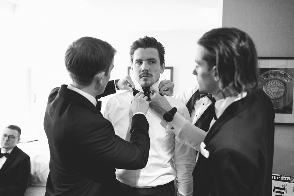 Groomsmen help groom tie his bowtie for his wedding ceremony