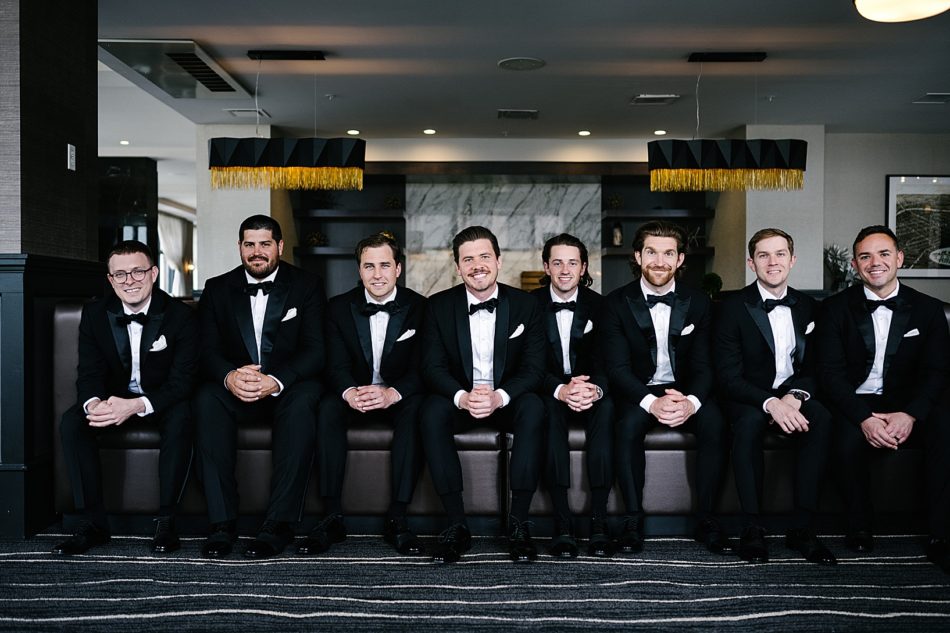 Groom and groom's party sit and smile in lobby of hotel