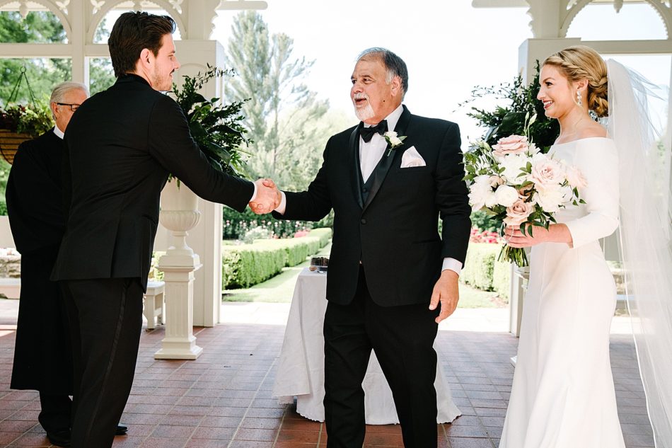 Groom shakes hands with father of the bride as he presents bride during ceremony