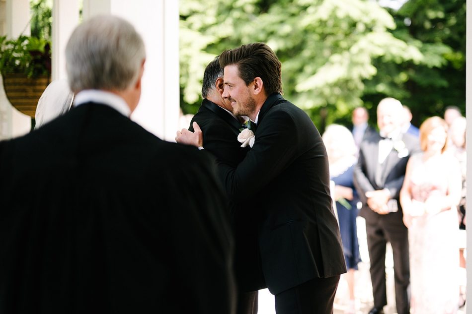 Groom hugs father of the bride as he presents bride during ceremony