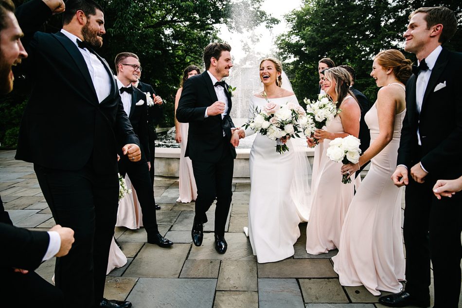 Bride and groom dance down aisle of wedding party in front of fountain