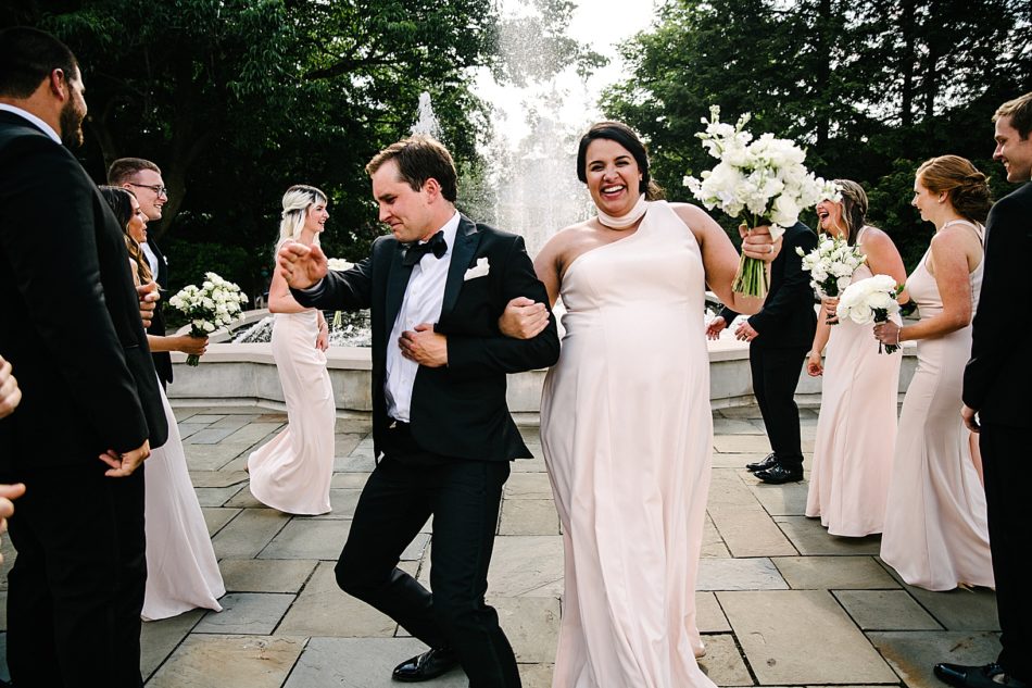 Groomsman and Bridesmaid dance down aisle of wedding party in front of fountain