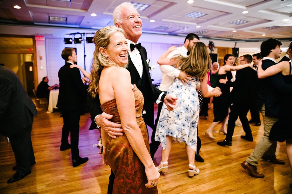 An older couple pose and smile while couples dance in the background