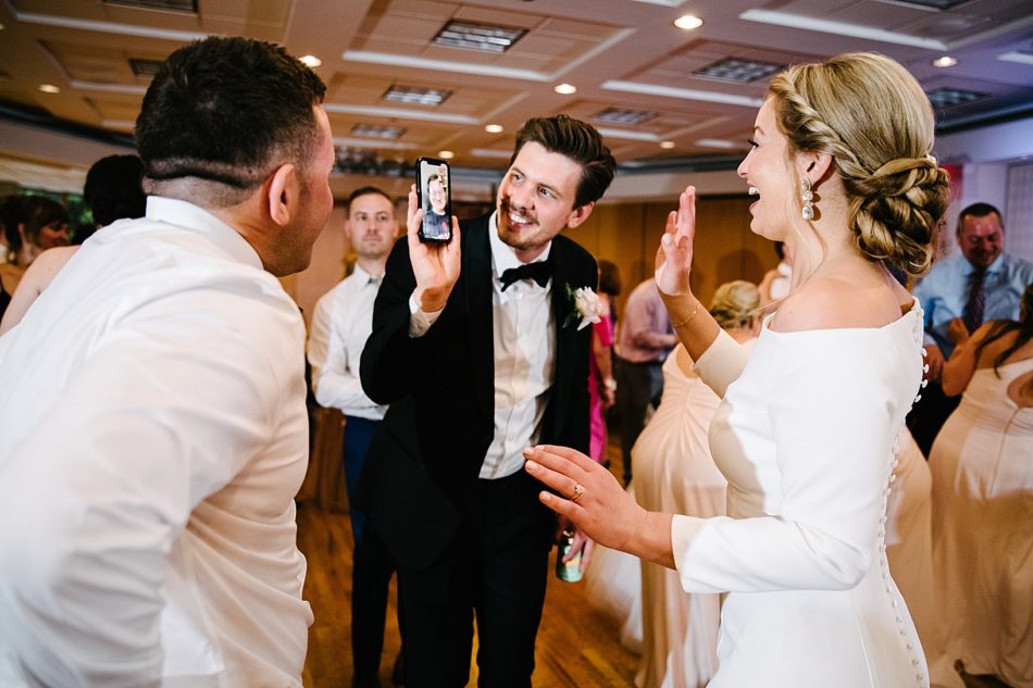 Groom holds up Facetime to bride who is smiling and waving