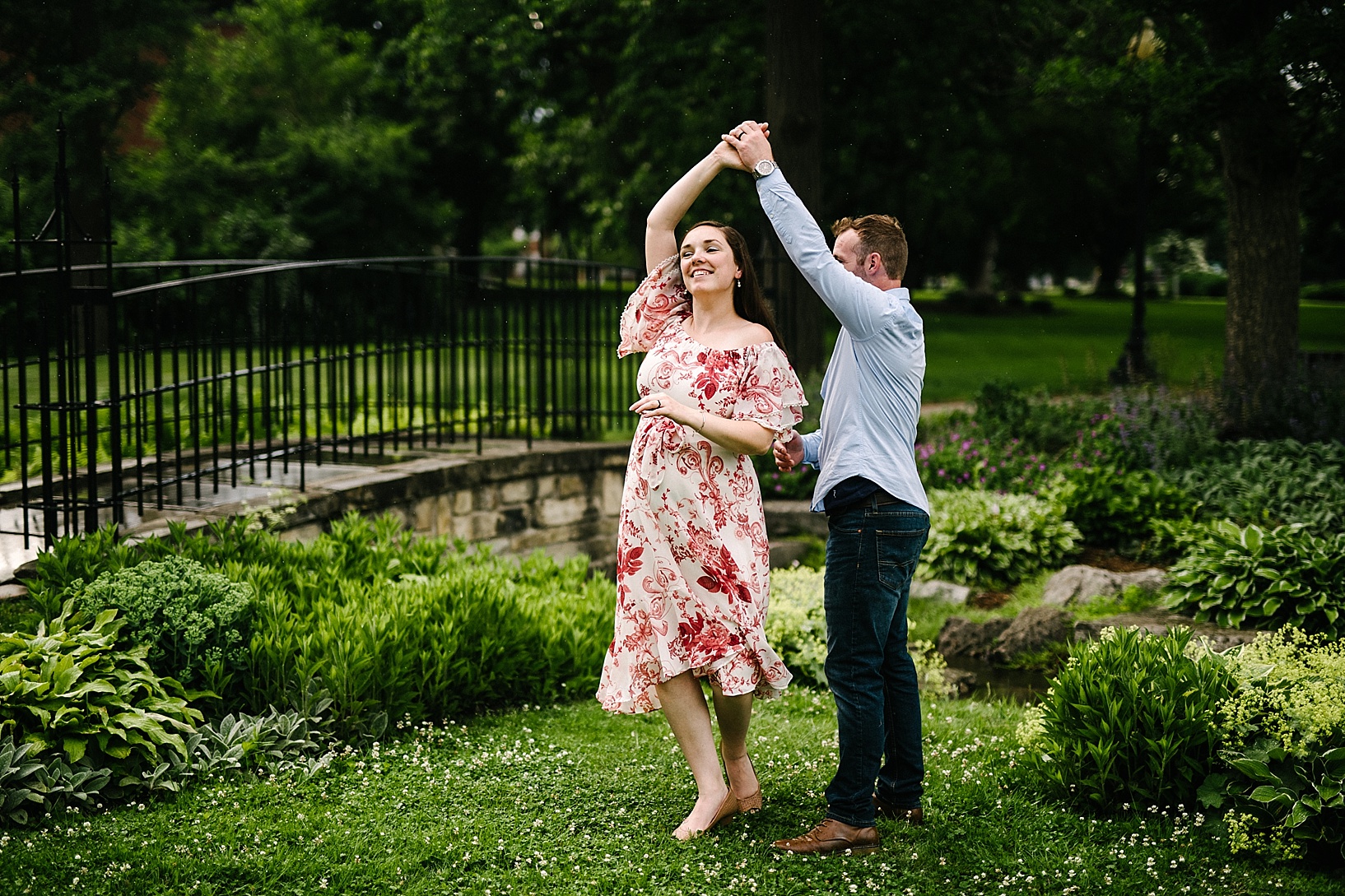 Husband twirls pregnant wife in a garden during rainy maternity session