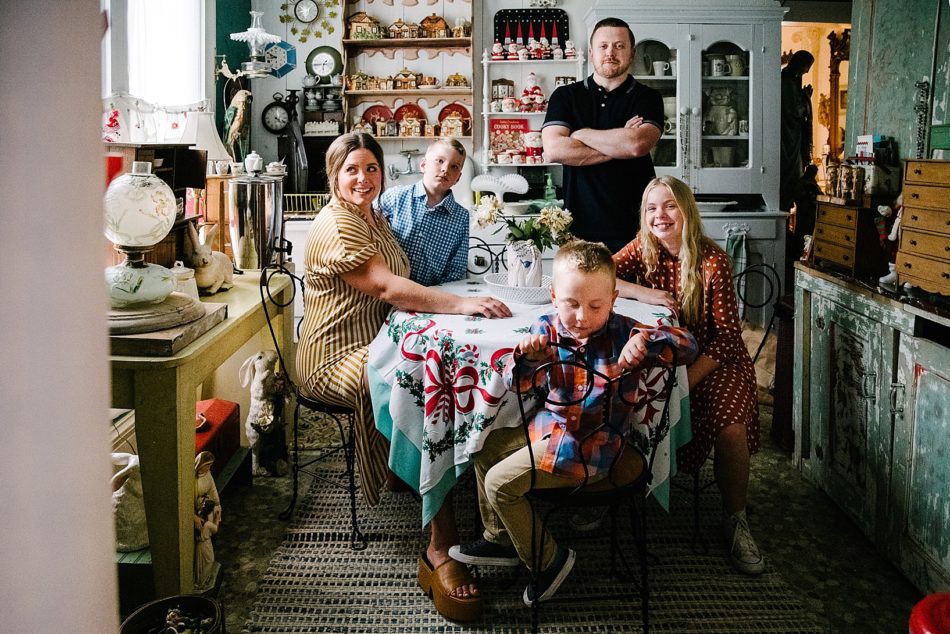 Family of five sits around kitchen table surrounded by trinkets and antiques