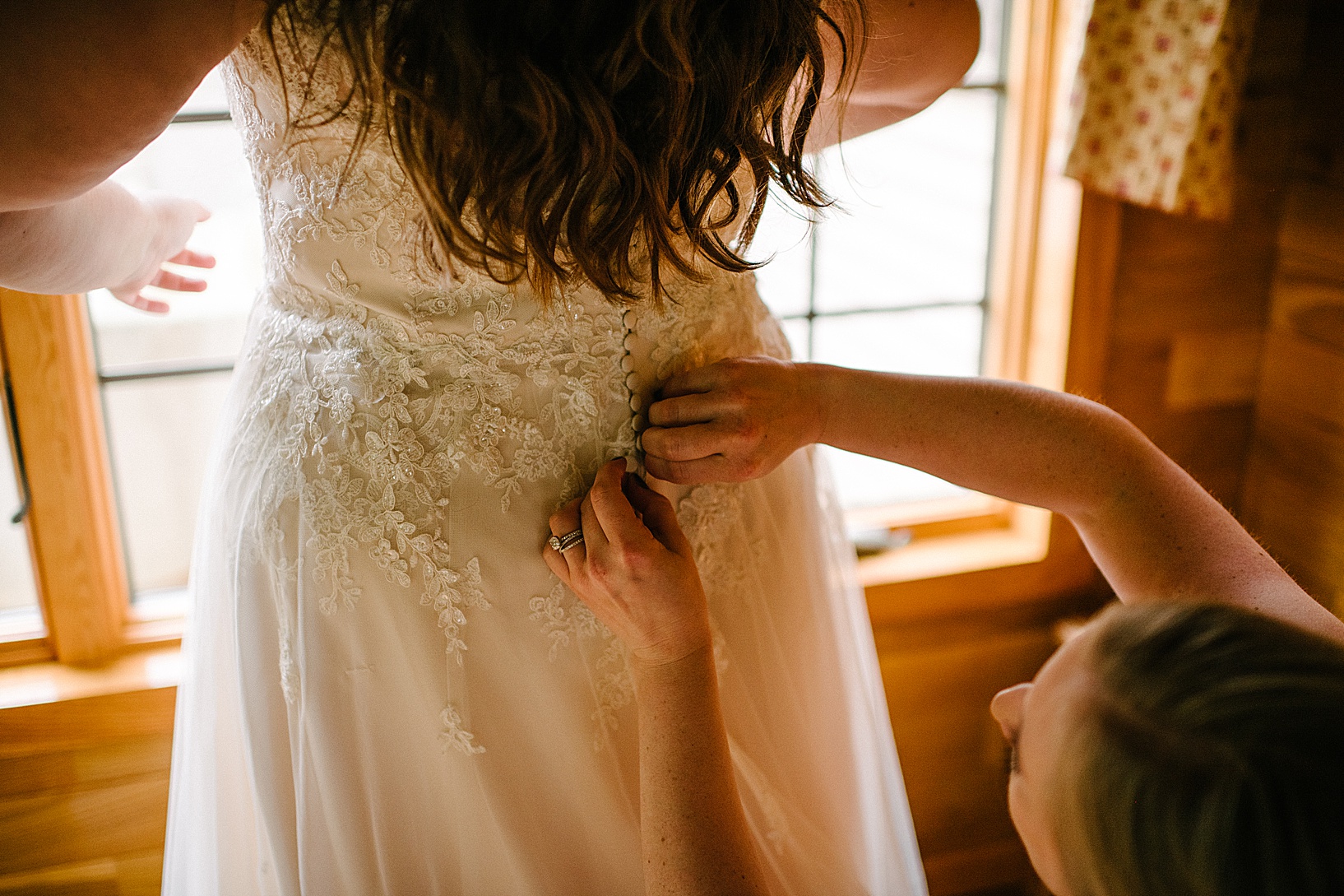 A bridesmaid helps the bride button up her wedding gown