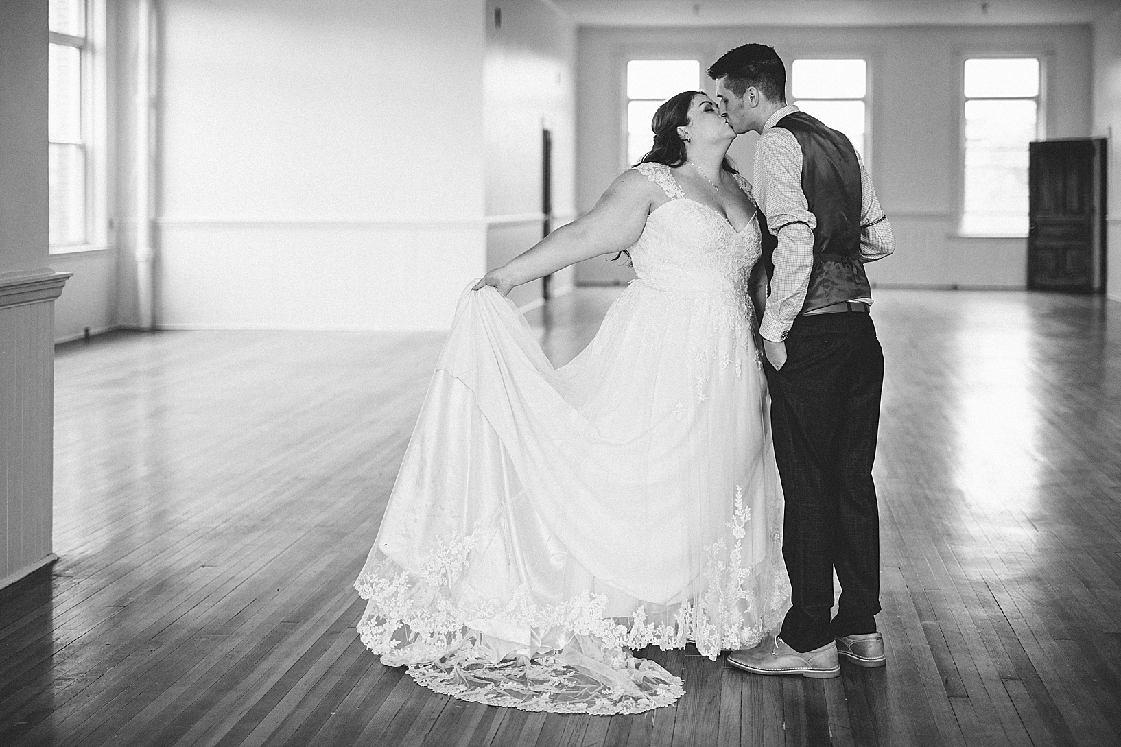 Bride and groom kiss in an empty room with wood floors