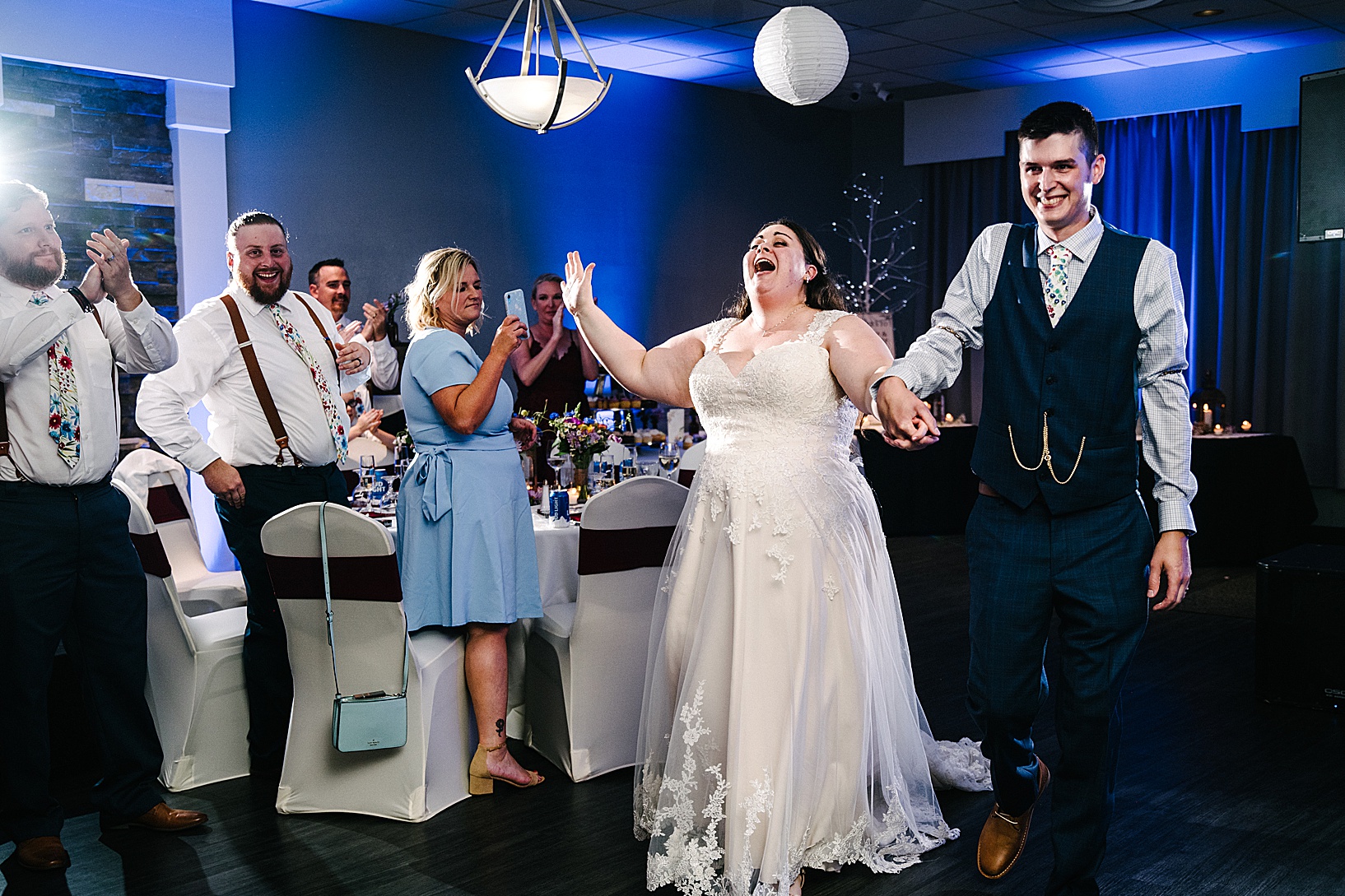 Guests stand and clap as bride and groom enter reception holding hands