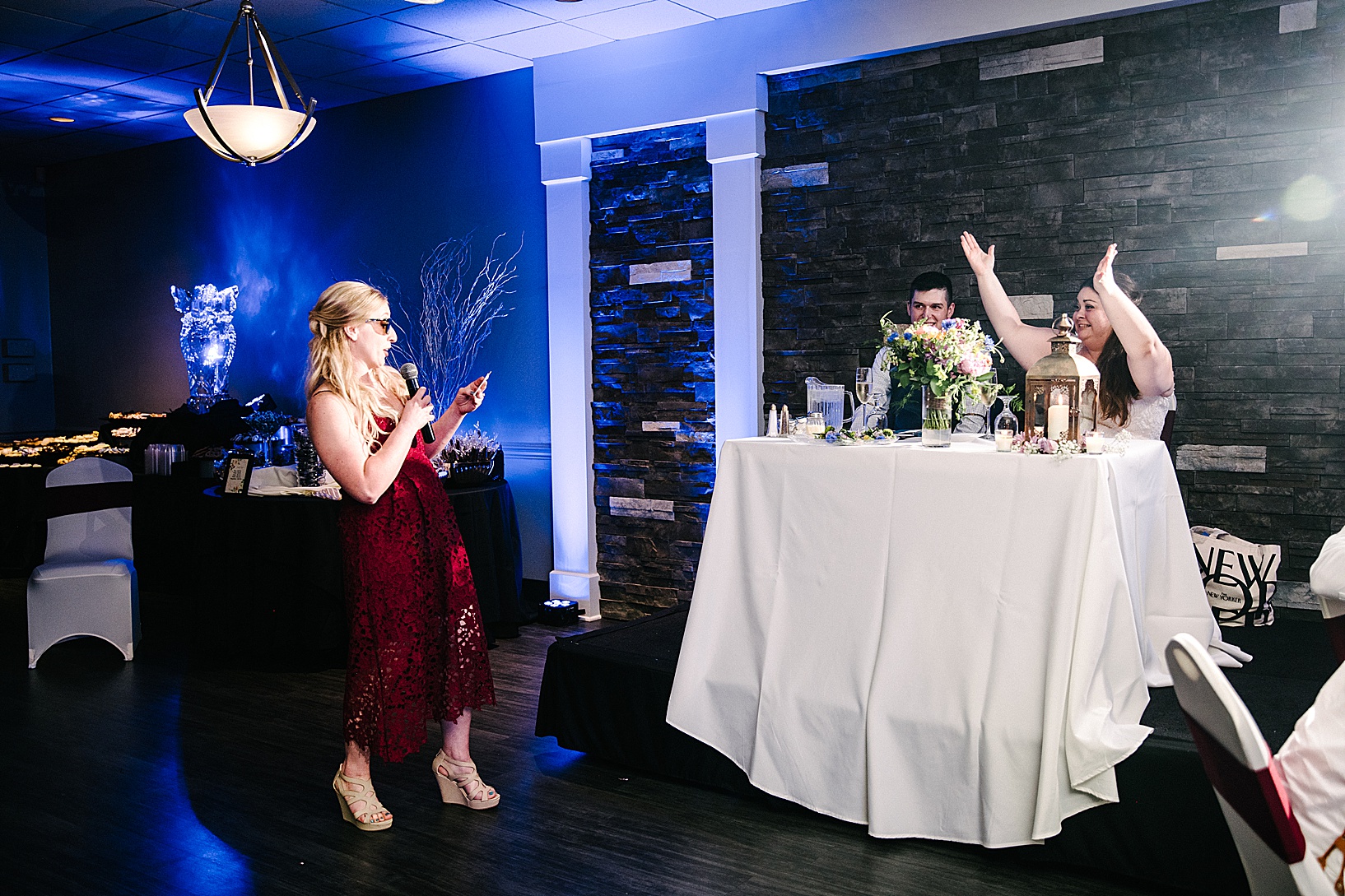 Bride claps with laughter as bridesmaid gives her speech wearing sunglasses