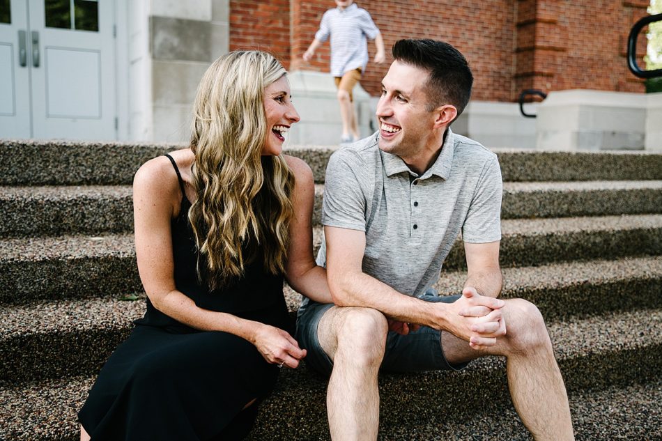 Man and woman sit on the steps of a building and smile at each other lovingly.