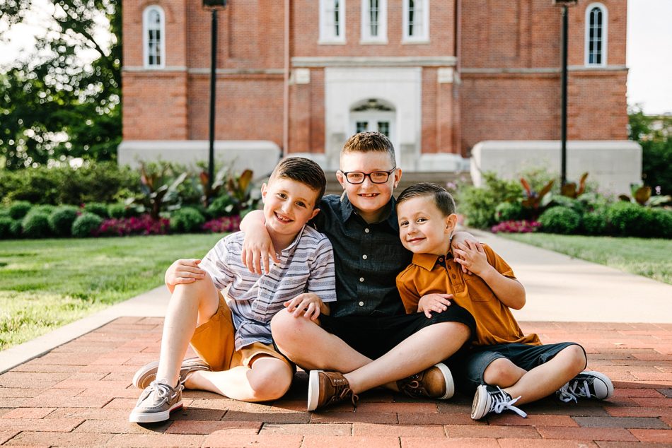Three brothers huddle together and smile in front of red brick building at Mount Union.