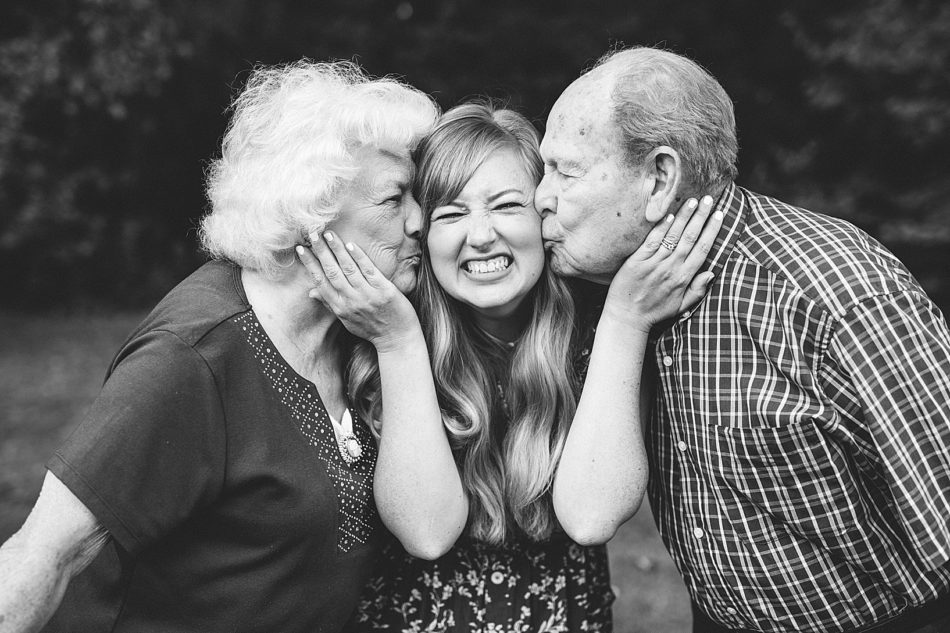Granddaughter in the middle being kissed on the cheek by grandma on one side and grandfather on the other side.