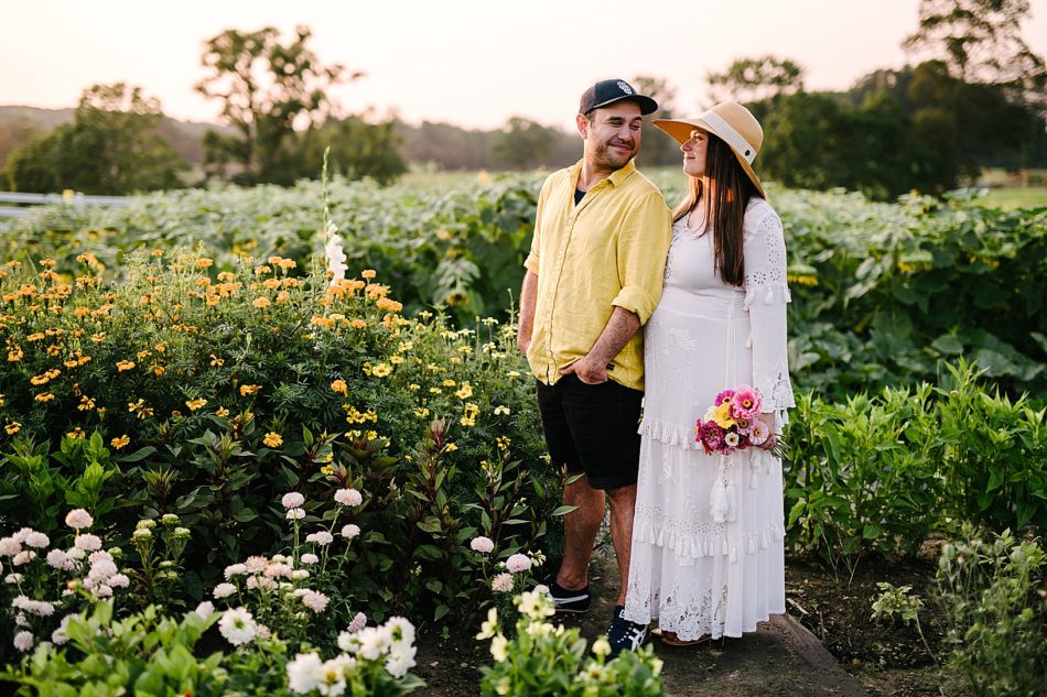 Man and pregnant wife smile at each other while standing in their flower farm