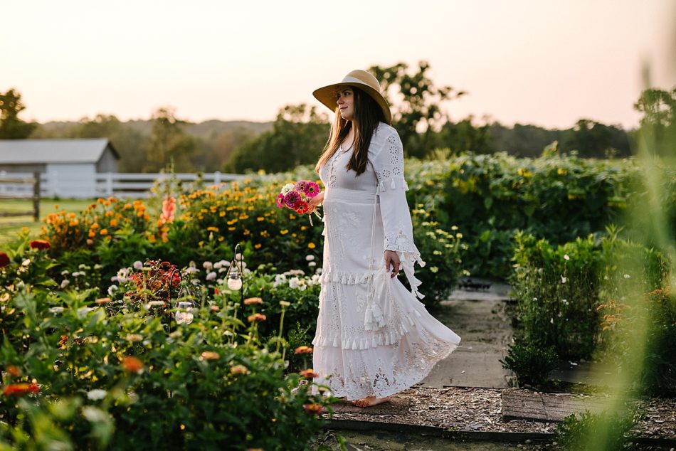 Pregnant woman walks barefoot through flower farm holding a bouquet of wildflowers