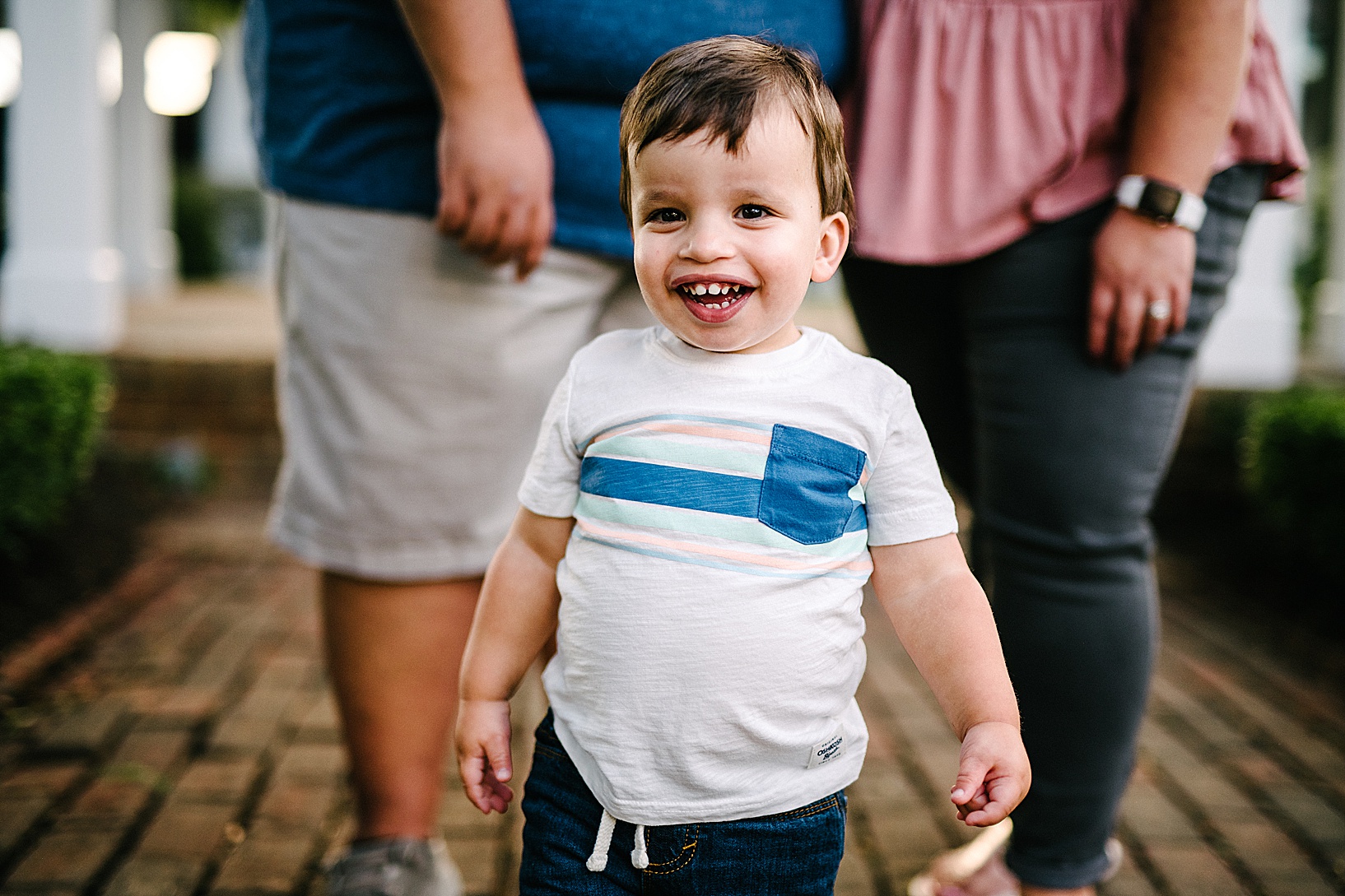 Young boy smiles at camera while his parents stand in the background