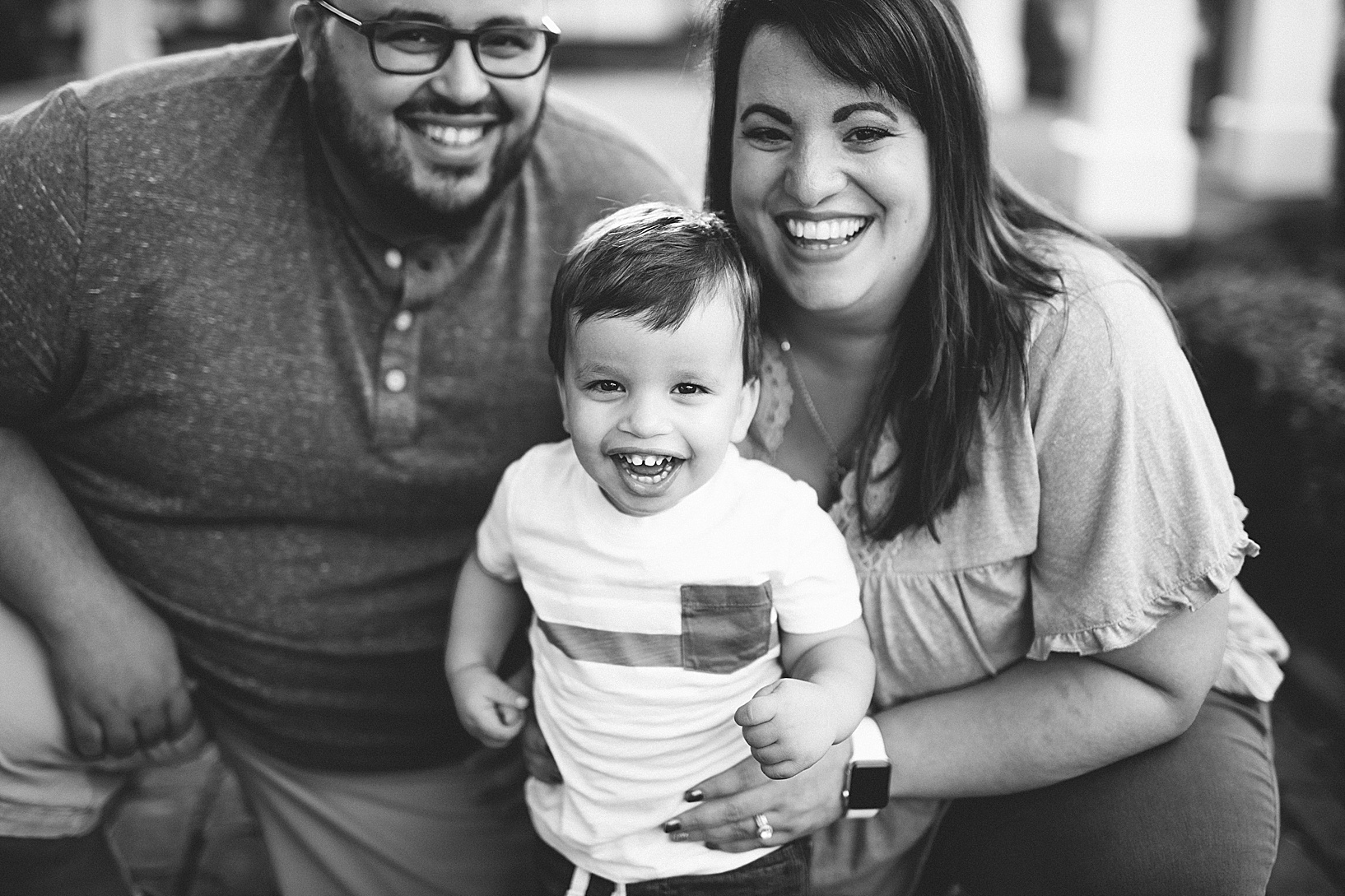 Man and woman crouch down next to their young son while all three smile at camera