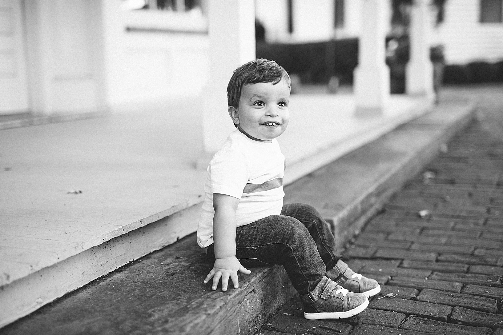 Little boy smiles and sits on wooden step on brick pathway at Western Village Reserve session