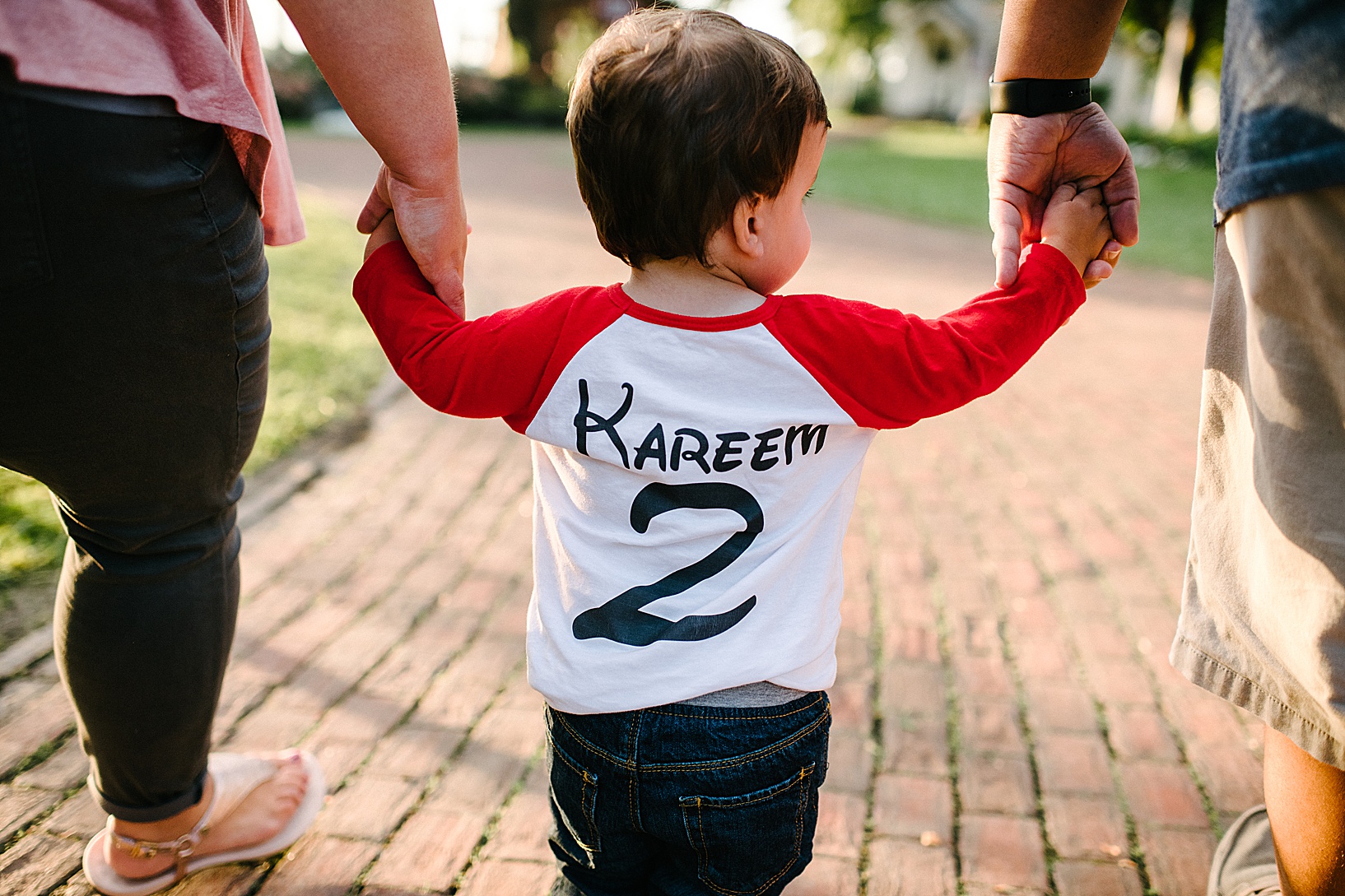 Back of little boy holding hands with his mom and dad, wearing a Disney font jersey that says "Kareem"
