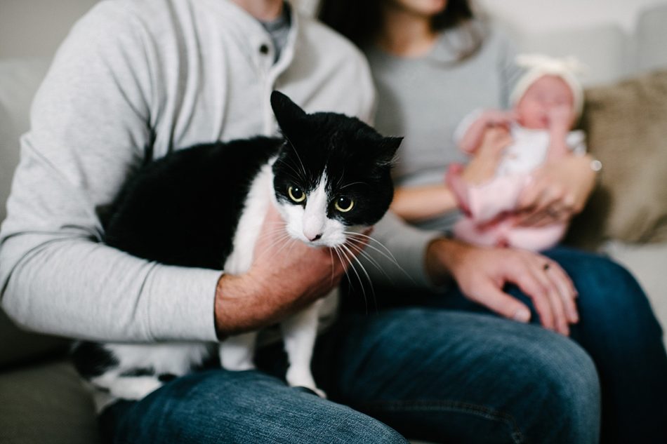 Man holding the families black and white cat with mom holding Baby Ava in the background
