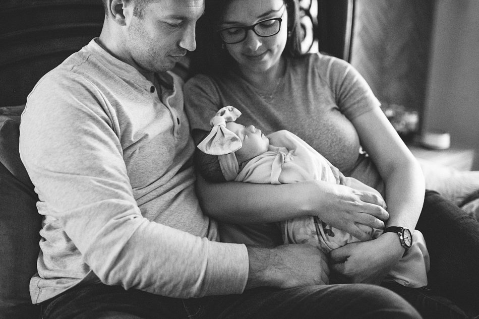 Woman and man cuddle newborn Baby Ava on their bed