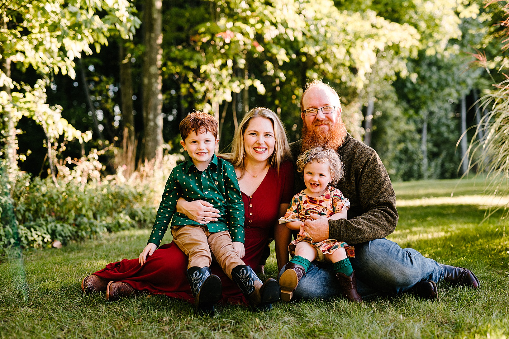 Woman and man sit on the grass while their son and toddler daughter sit on their laps in the grass during fall family session