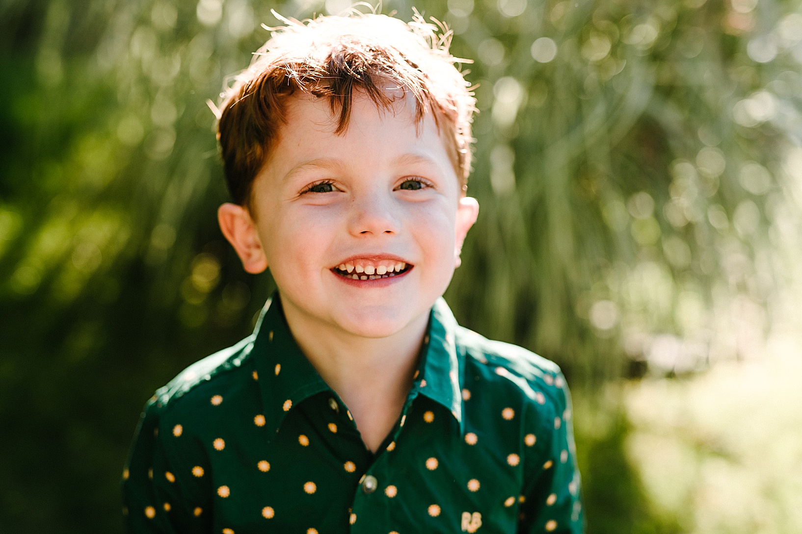 Red-headed boy in green polka dot shirt smiles at the camera