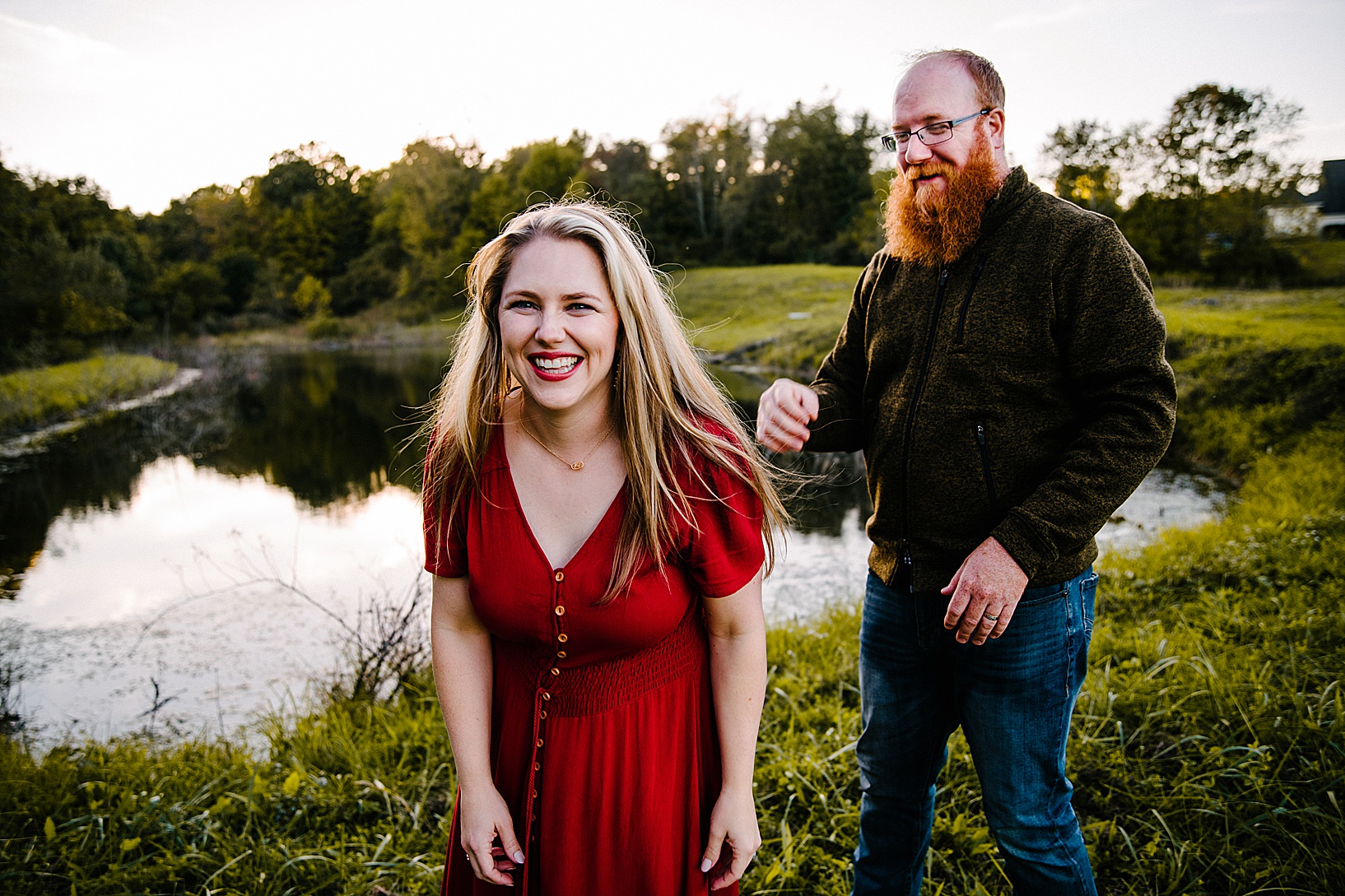 Blonde woman laughs while walking away from red headed husband in front of dreamy lake fall family session