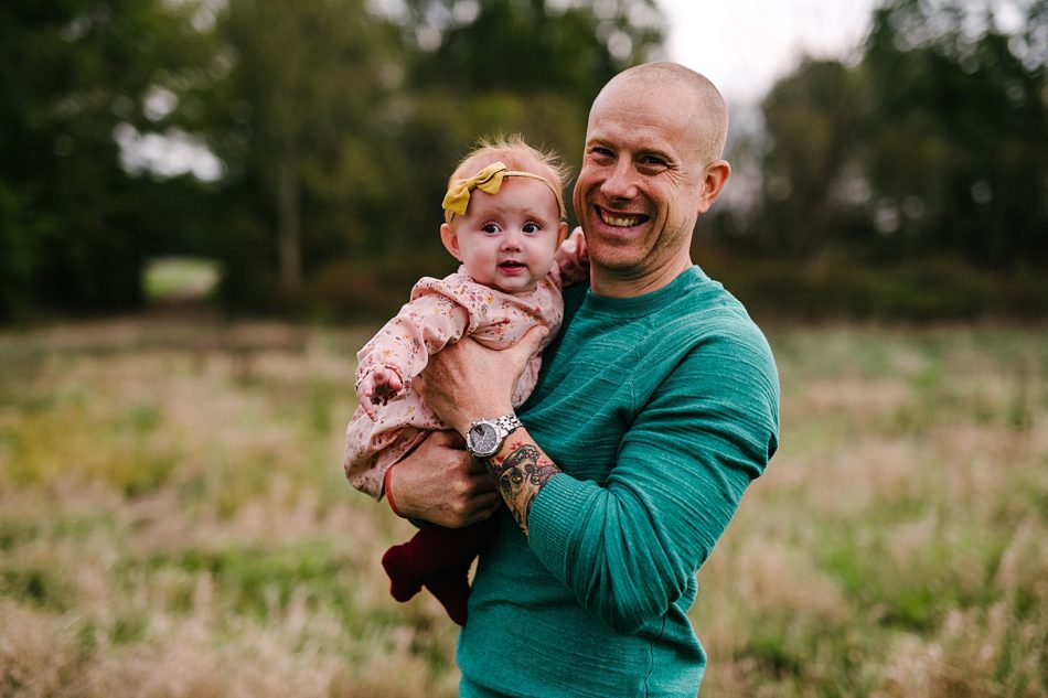 Man holds his baby girl with a huge yellow head bow with a huge grin on his face.