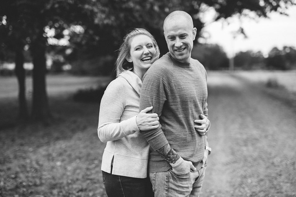 Blonde woman hugs her husband from behind and smiles as they stand on a country gravel road in North Jackson, Ohio.