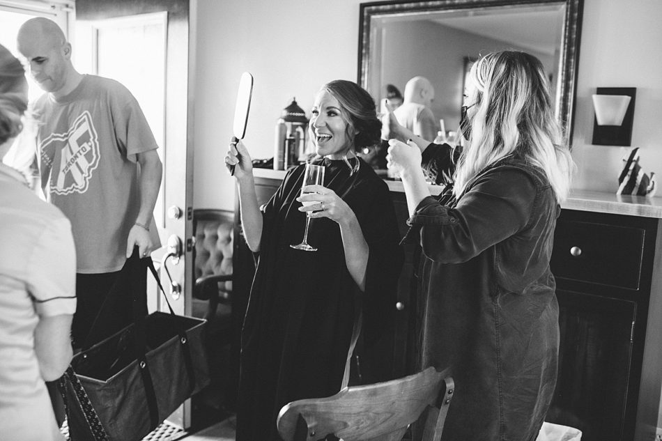 Bride admires her hair in a hand mirror while holding a glass of champagne