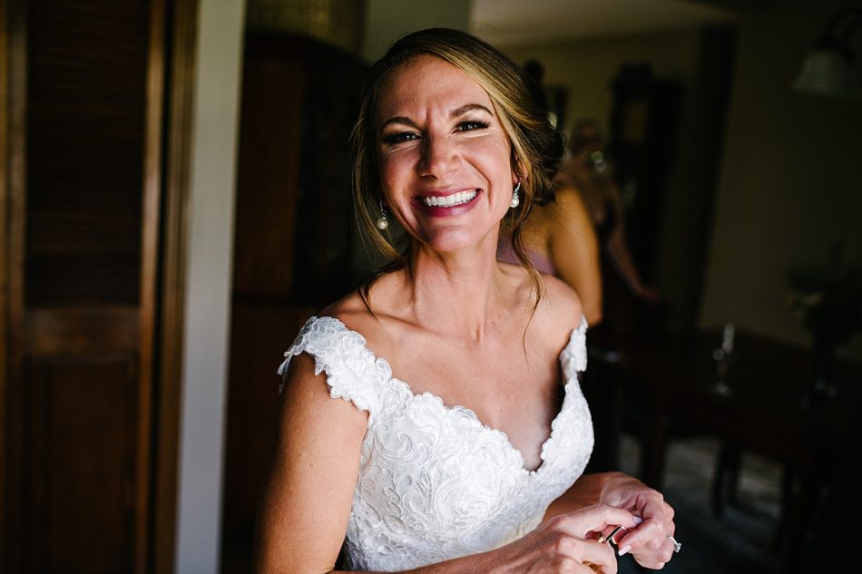 Bride smiles at camera while holding her lipstick in her hands