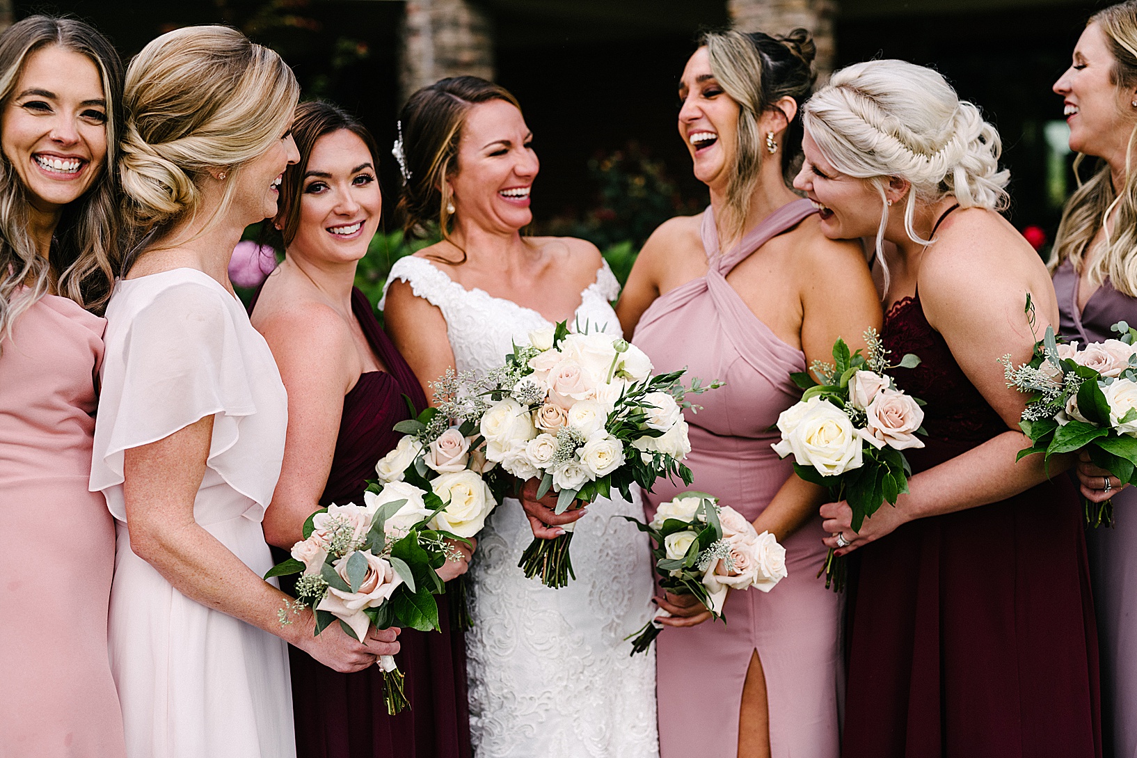 Bride and bridal party gather and laugh while holding their bouquets