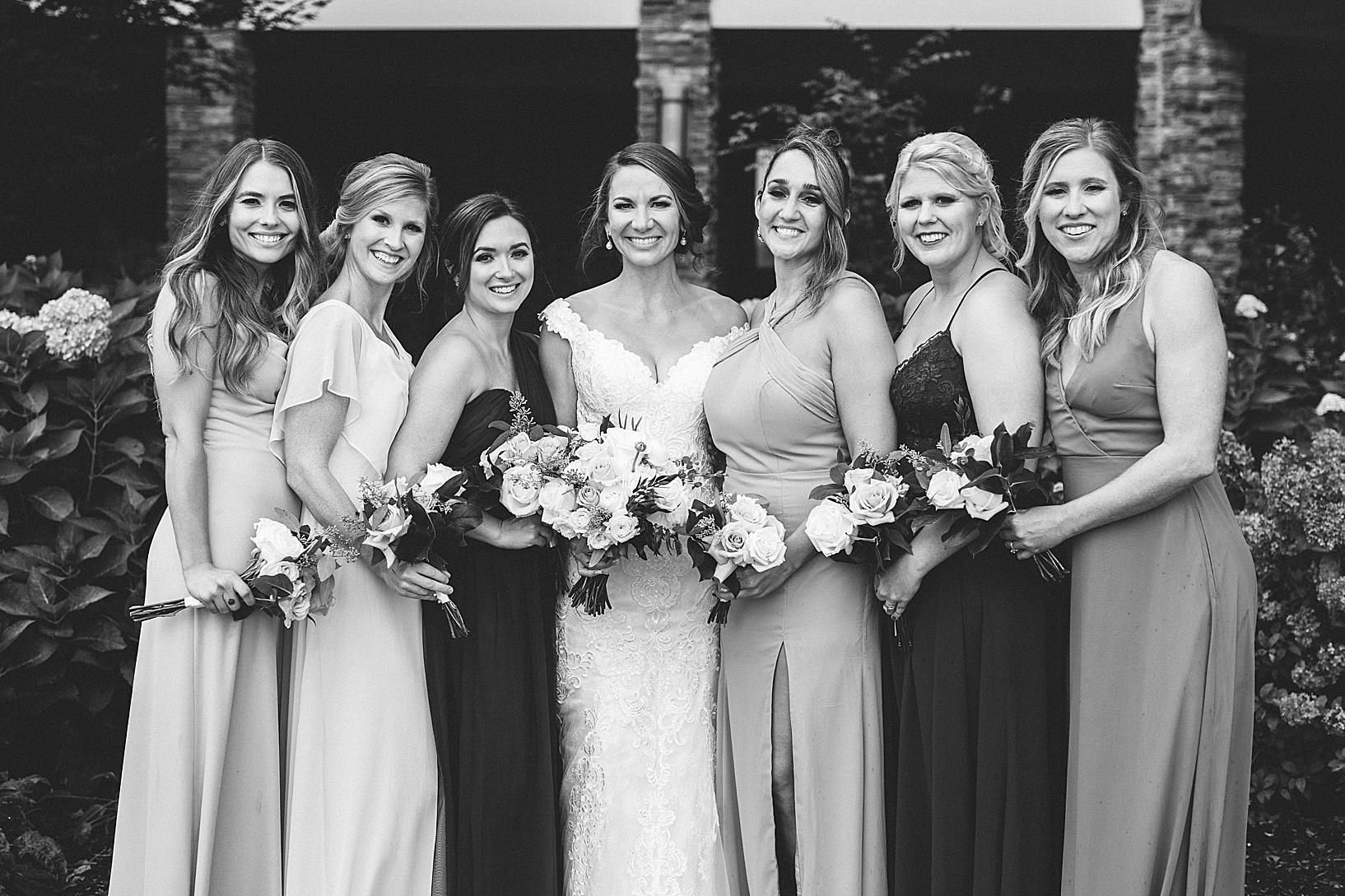 The bridal party stands and smiles while holding their bouquets