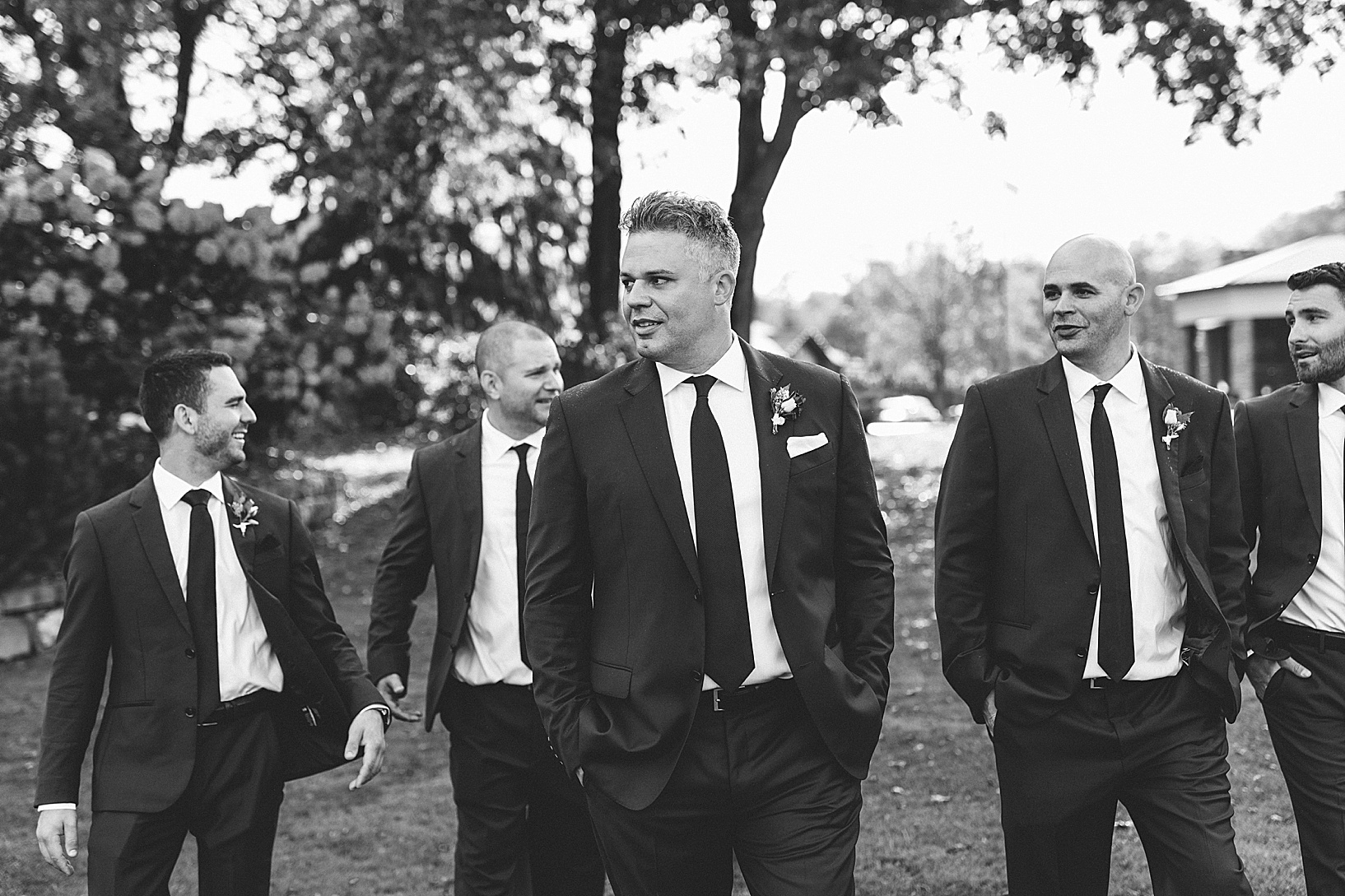 The groom and groomsmen walking on the lawn of the Lake Club with their hands in their suit pockets.