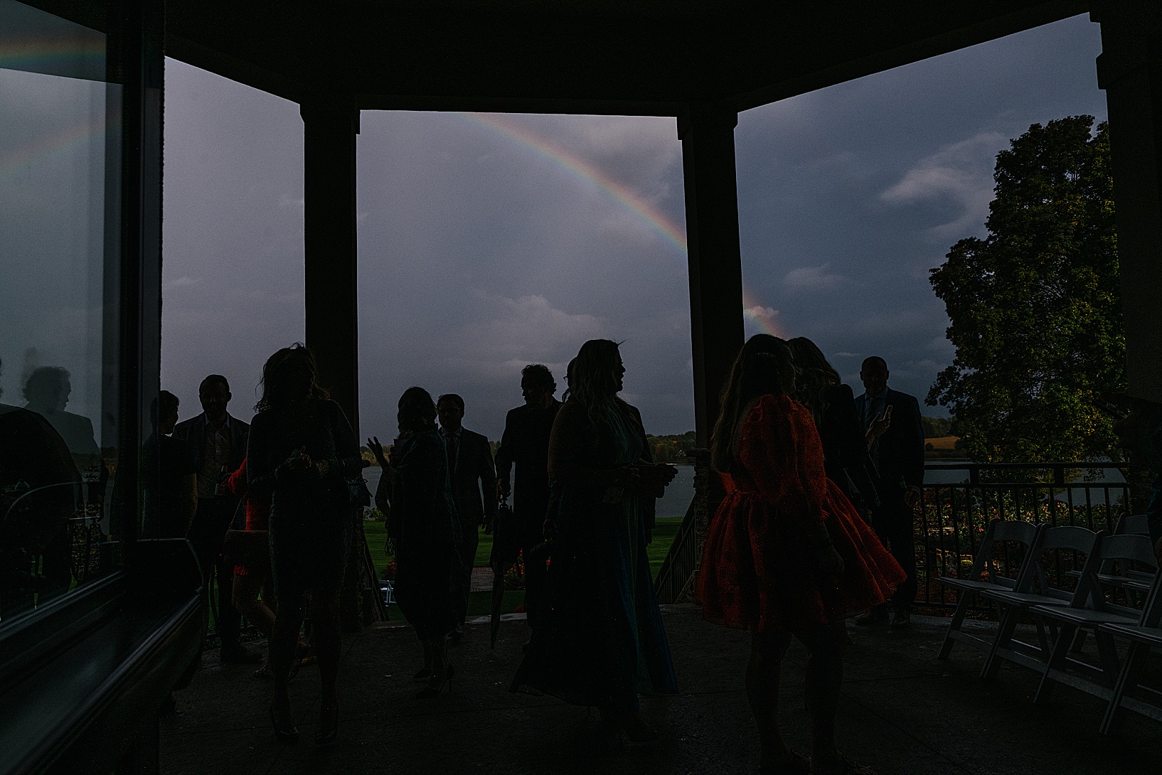 Guests under the lake club pavilion as a rainbow appears in the stormy sky.