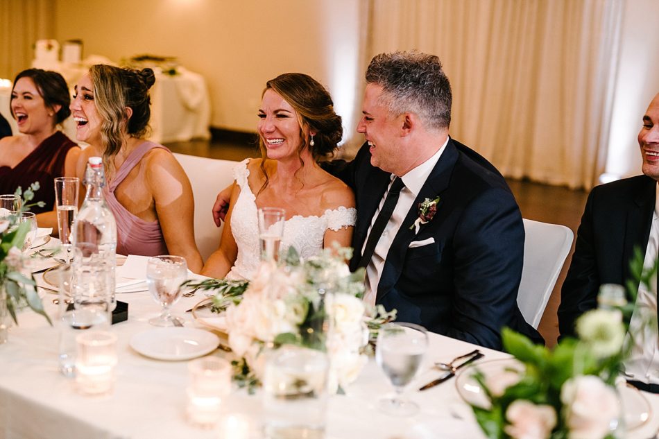 The maid of honor and bride laughing while the groom looks at her and laughs.