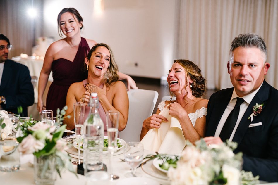 Bride and bridesmaid laugh together at the dinner table.