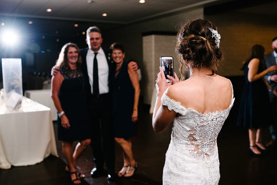 Bride taking photo of guests and the groom with an iphone.