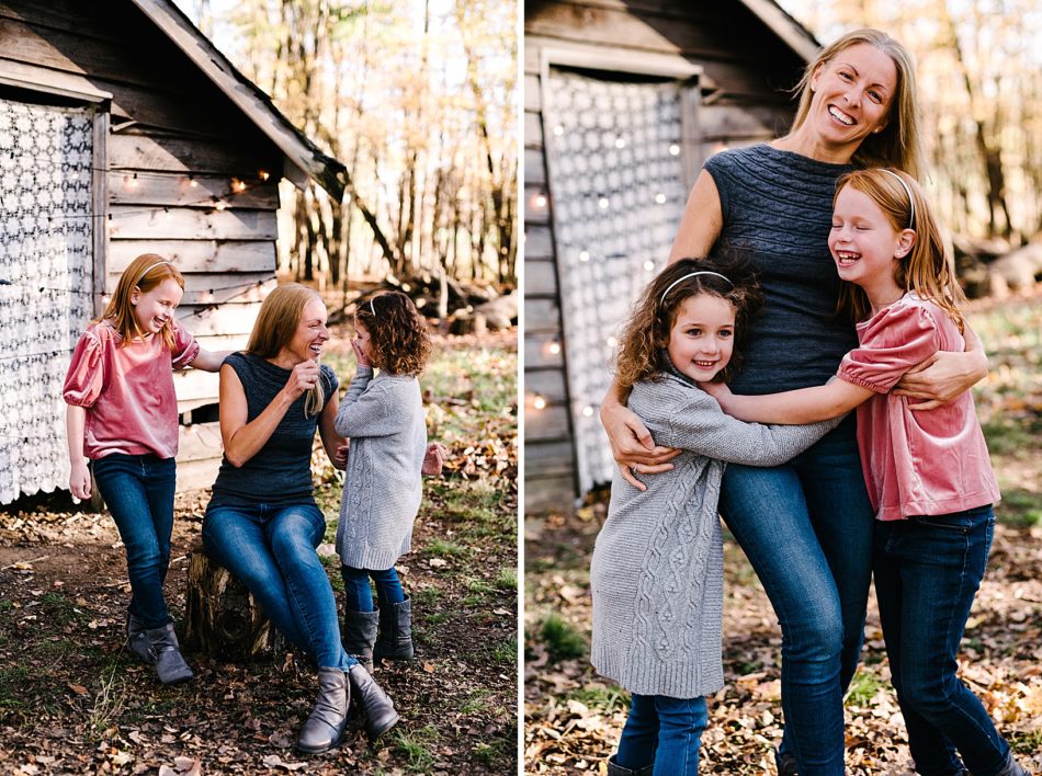 Woman sits on a tree stump with her daughters on either side of her as she laughs and one daughter covers her hand with her mouth.
