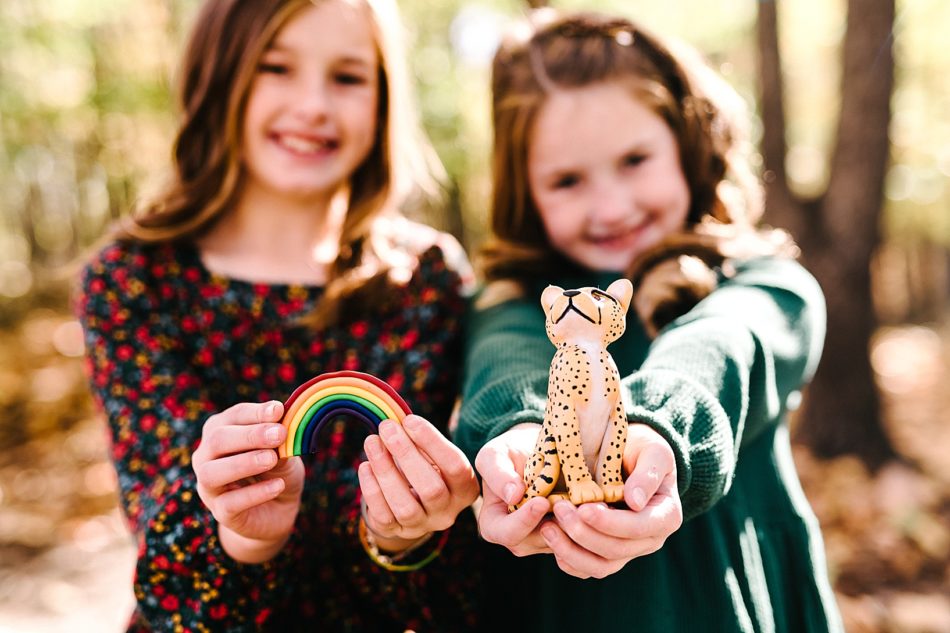 Two redhead girls show off their trinkets to the camera, one holding a clay rainbow and the other holding a clay cheetah.
