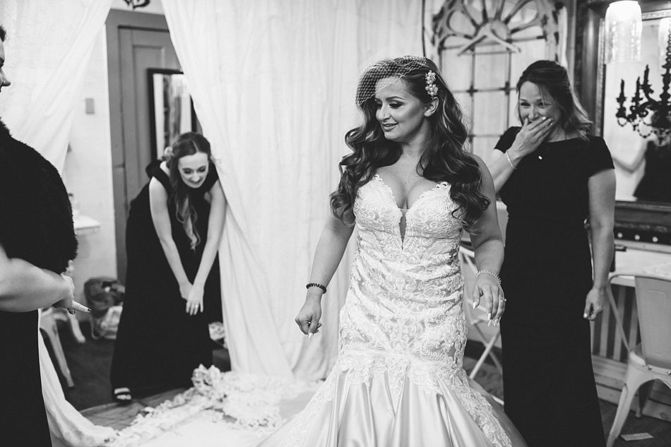 The bride in her gown walking by and a woman in the background smiling and holding her hand over her mouth.