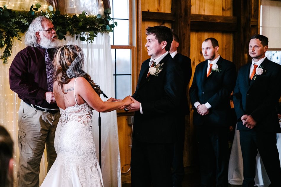 Bride and groom hold hands at the altar with groomsmen standing in the background.