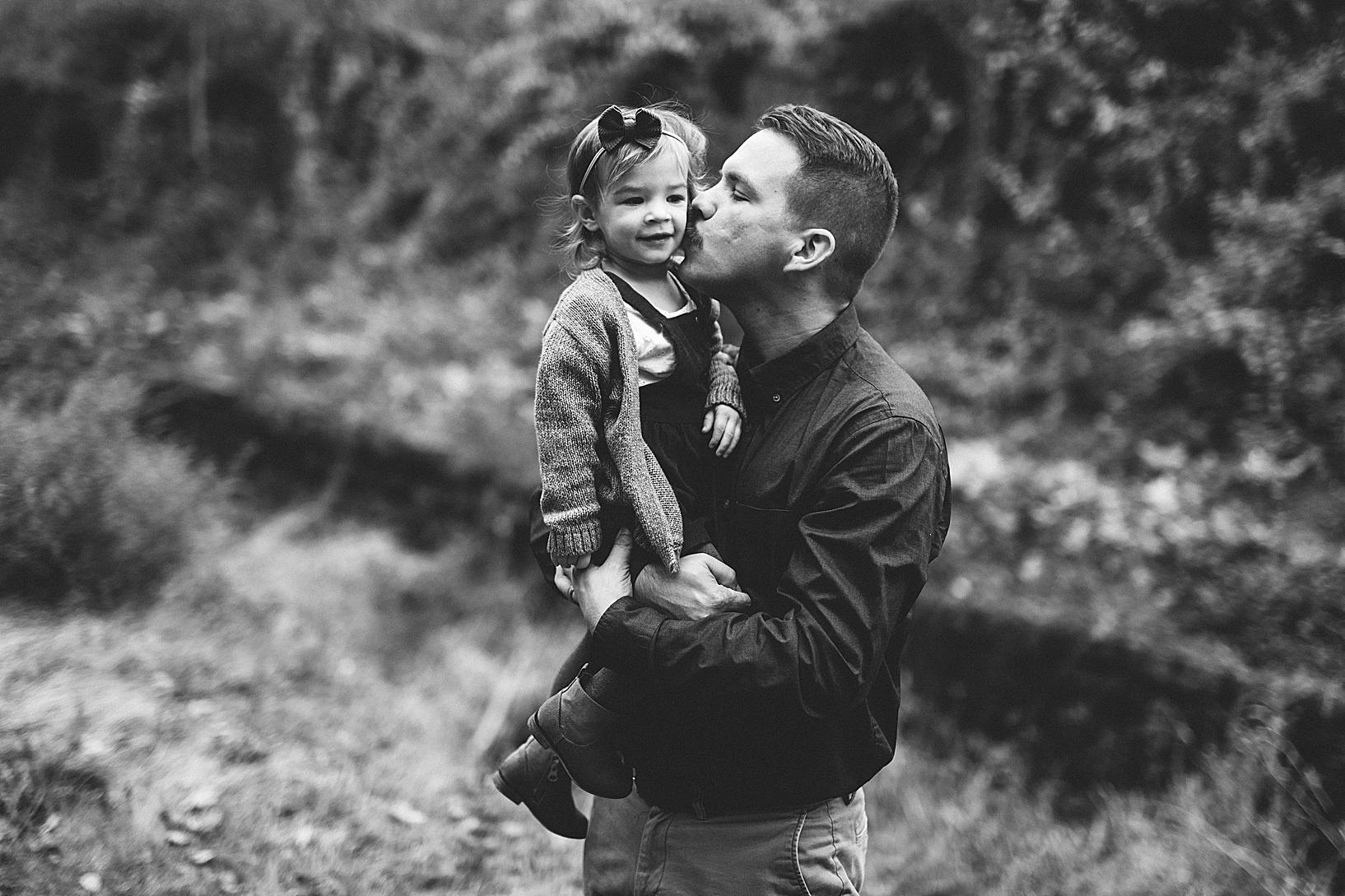 Brunette man kisses his daughter on the cheek as he holds her.