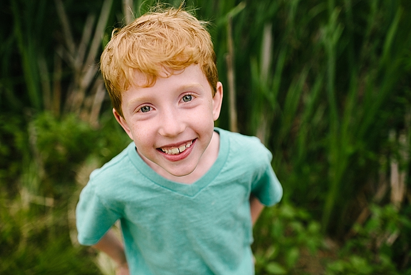 redhead boy with freckles and blue eyes standing in tall grass