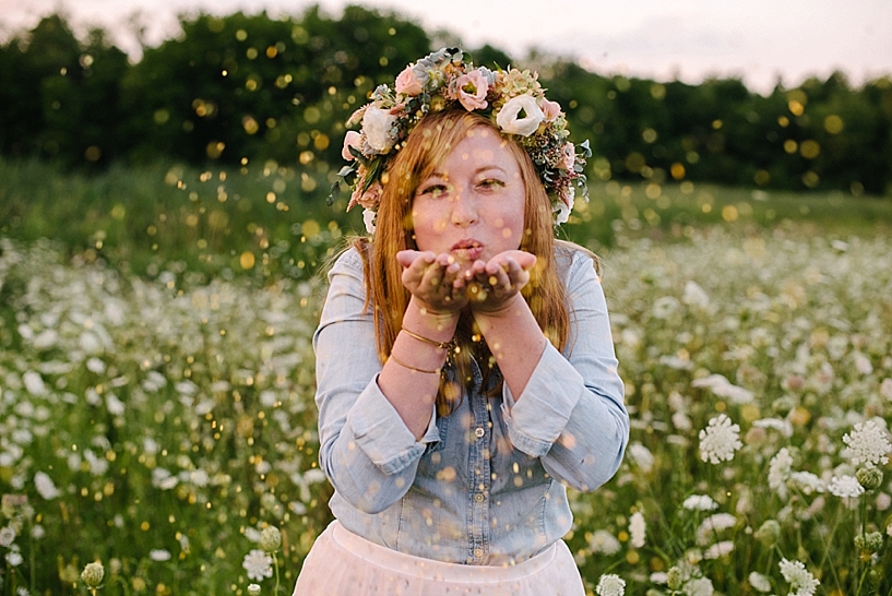 Redheaded woman wearing a flower crown blowing glitter at the camera