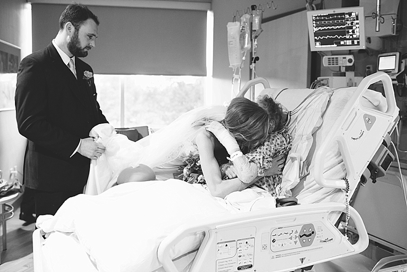 bride hugging grandmother in hospital bed with husband standing nearby