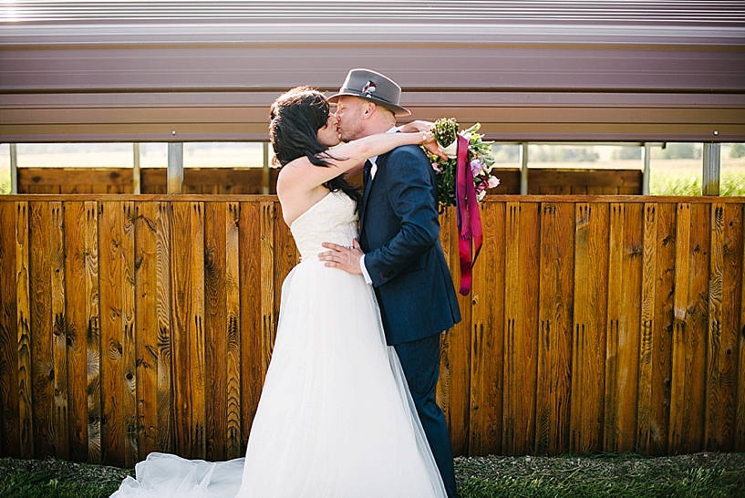 bride and groom kissing by wooden barn