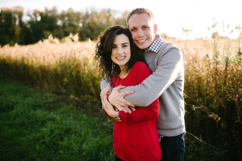 woman in red sweater with curly hair and husband in grey sweater hugging