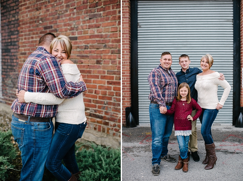 husband in plaid hugging wife in cream sweater by brick wall